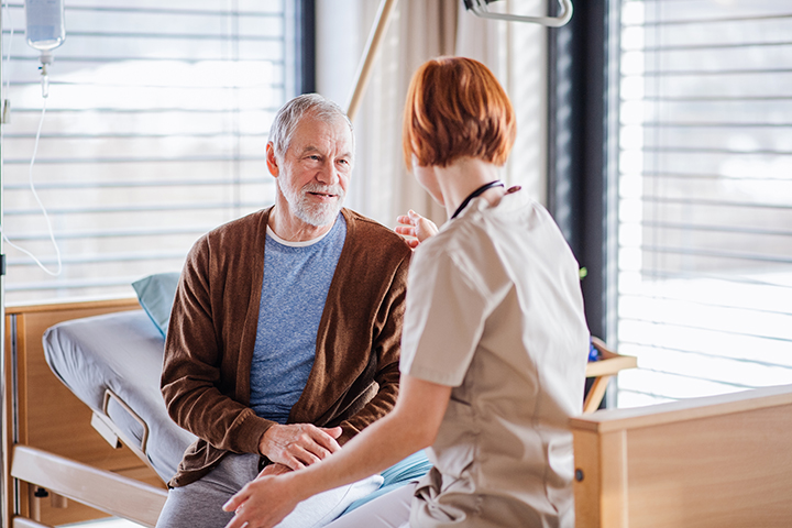 A female doctor talking to senior patient in bed in hospital.